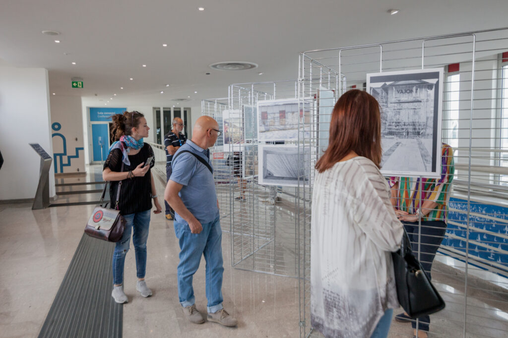 Two ladies and a gentleman looking at photos displayed in an exhibition in memory of Vajont